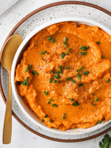 Vegan sweet potato mash in a bowl with fresh green herbs and a gold spoon.