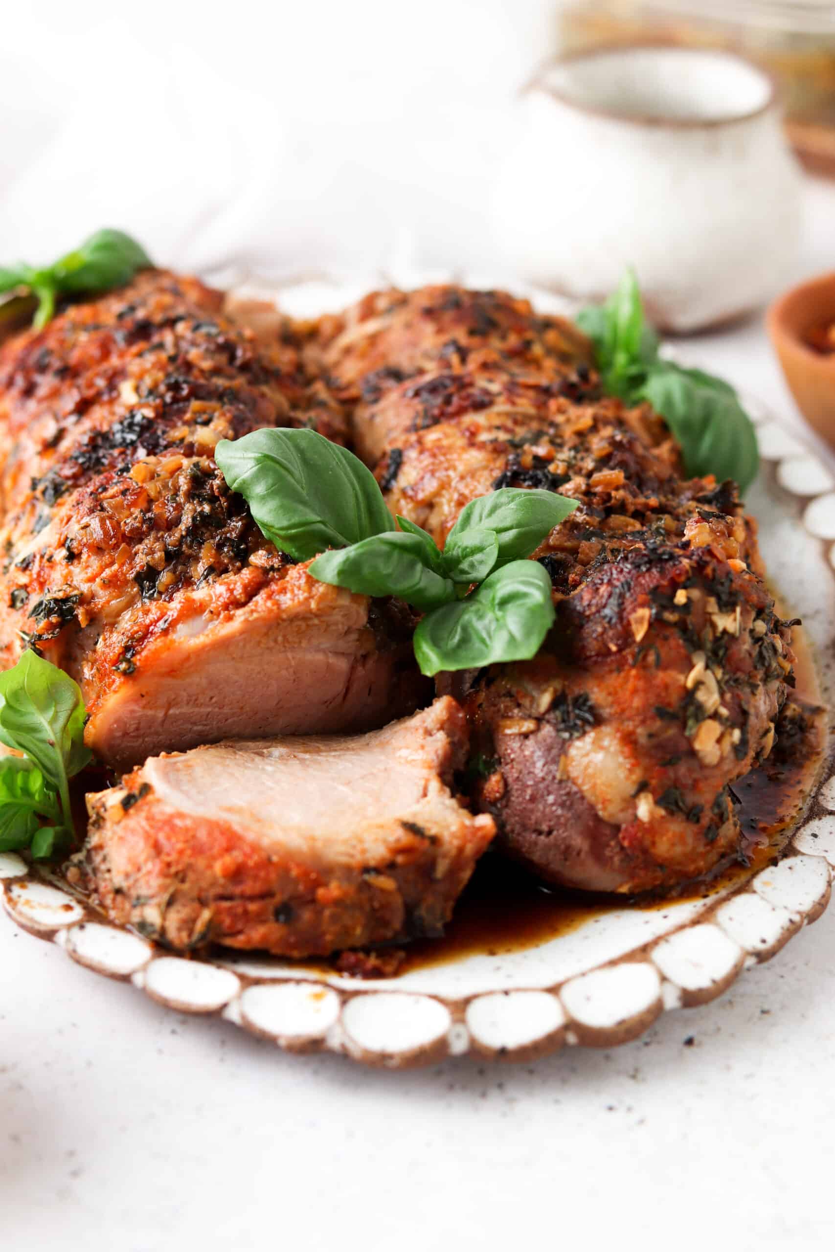 Whole30 pork tenderloin with herb crust sliced on a white platter and garnished with fresh green basil.