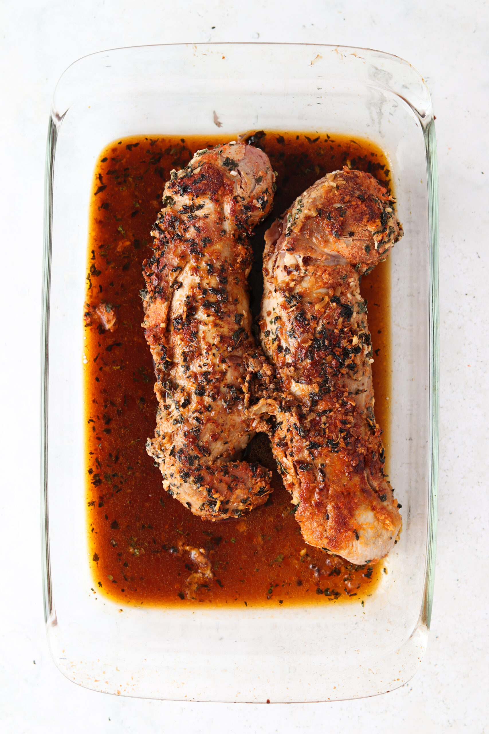 Two herb crusted pork tenderloin resting in a glass casserole dish.