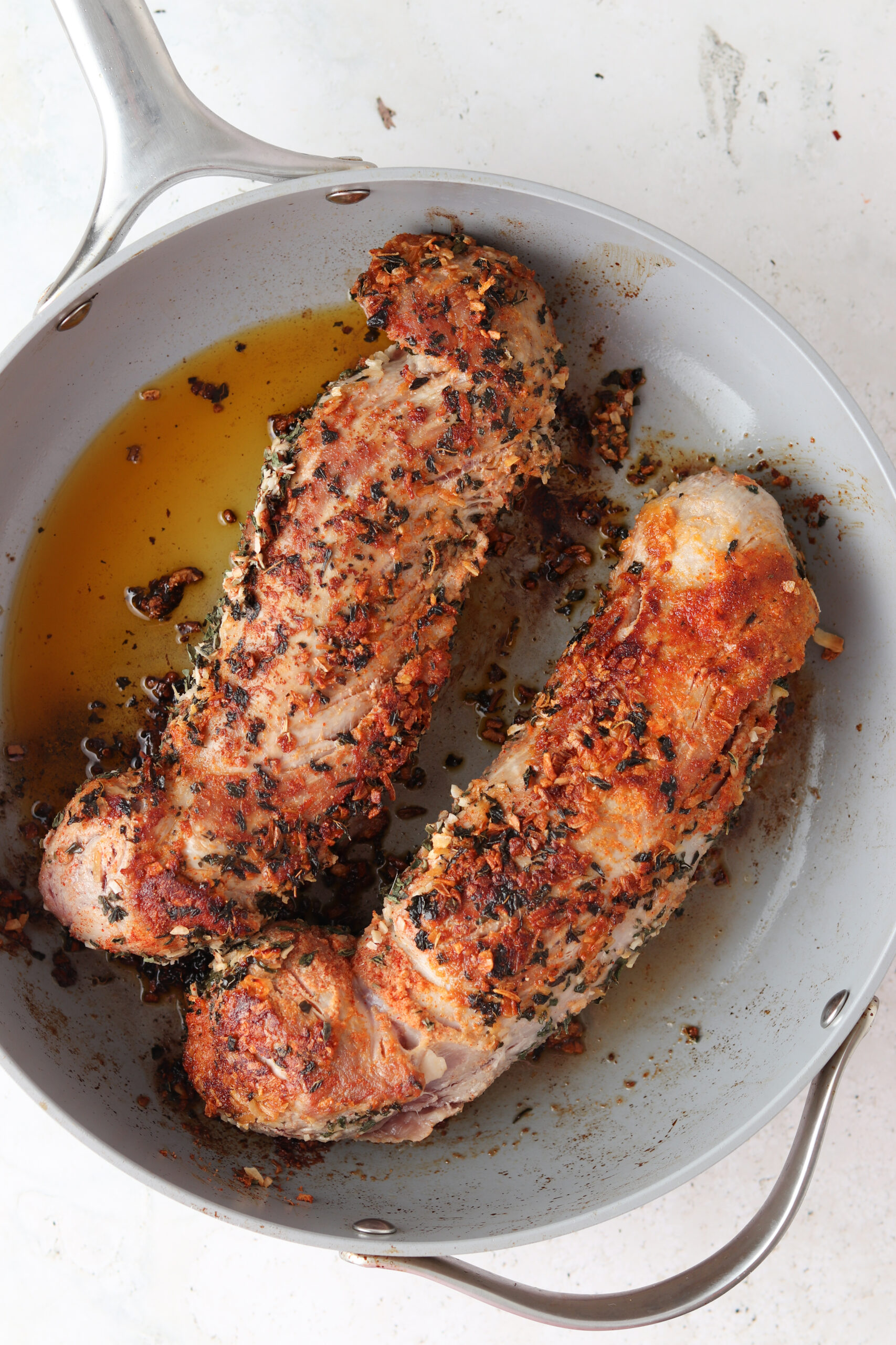 Two seared herb crusted pork tenderloins in a pan.