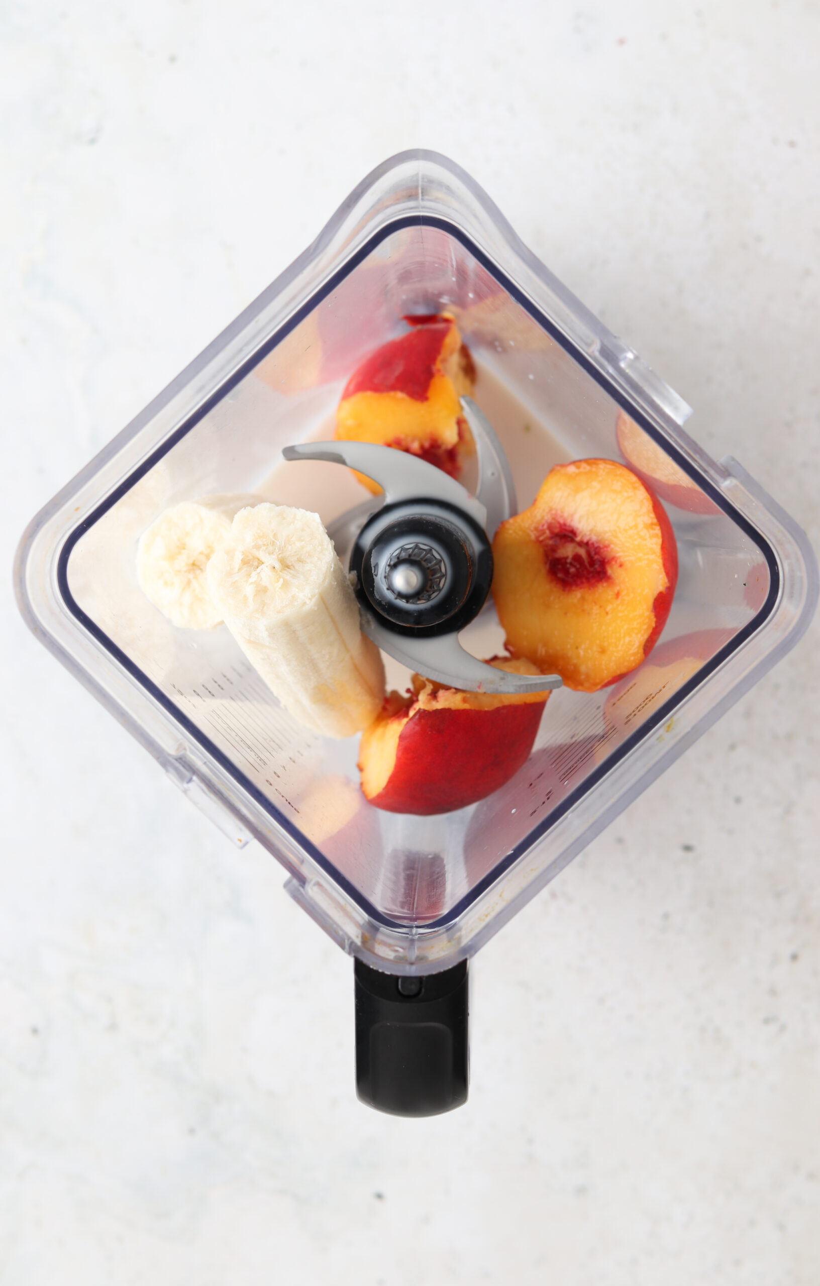 Banana peach smoothie ingredients in a blender base.