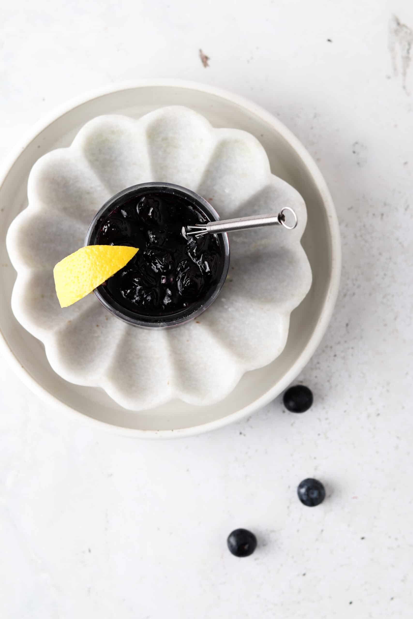 Blueberry maple jam in a cup and garnished with a lemon wedge on a platter.