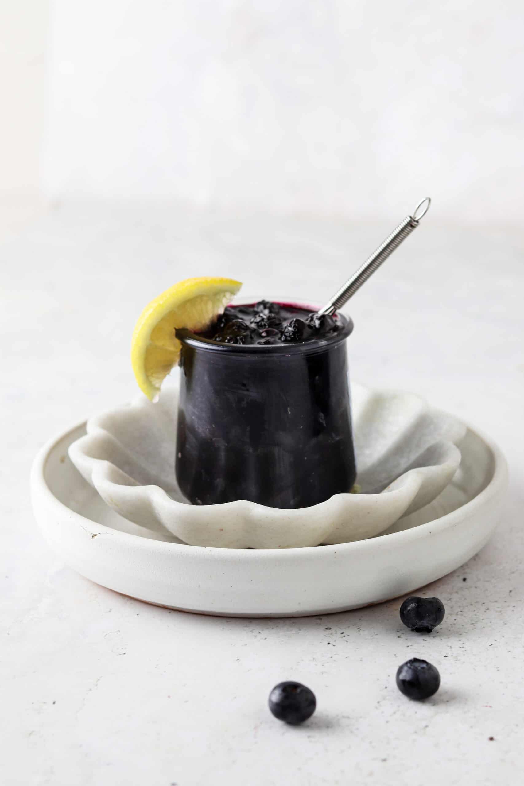 Blueberry maple jam in a jar with a lemon wedge and small whisk.