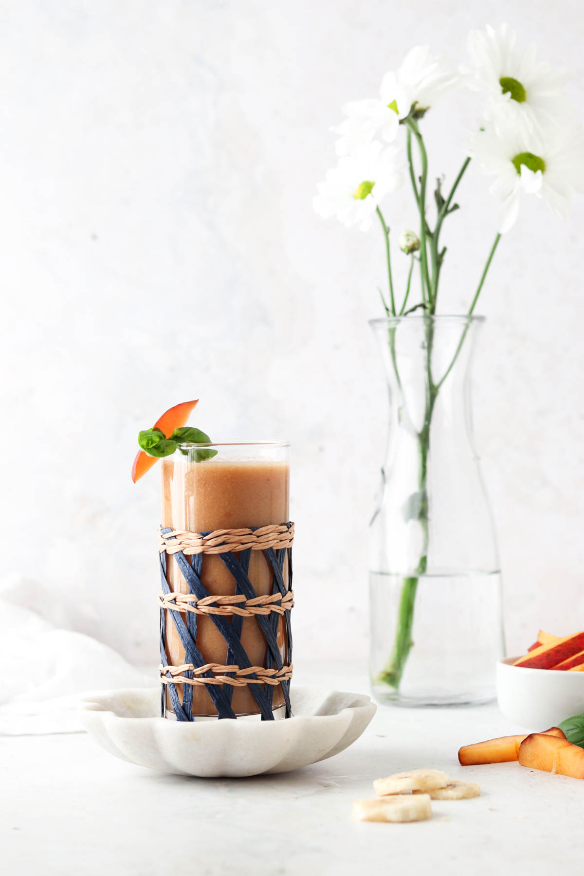 Banana peach smoothie in a glass with flowers in the background. 