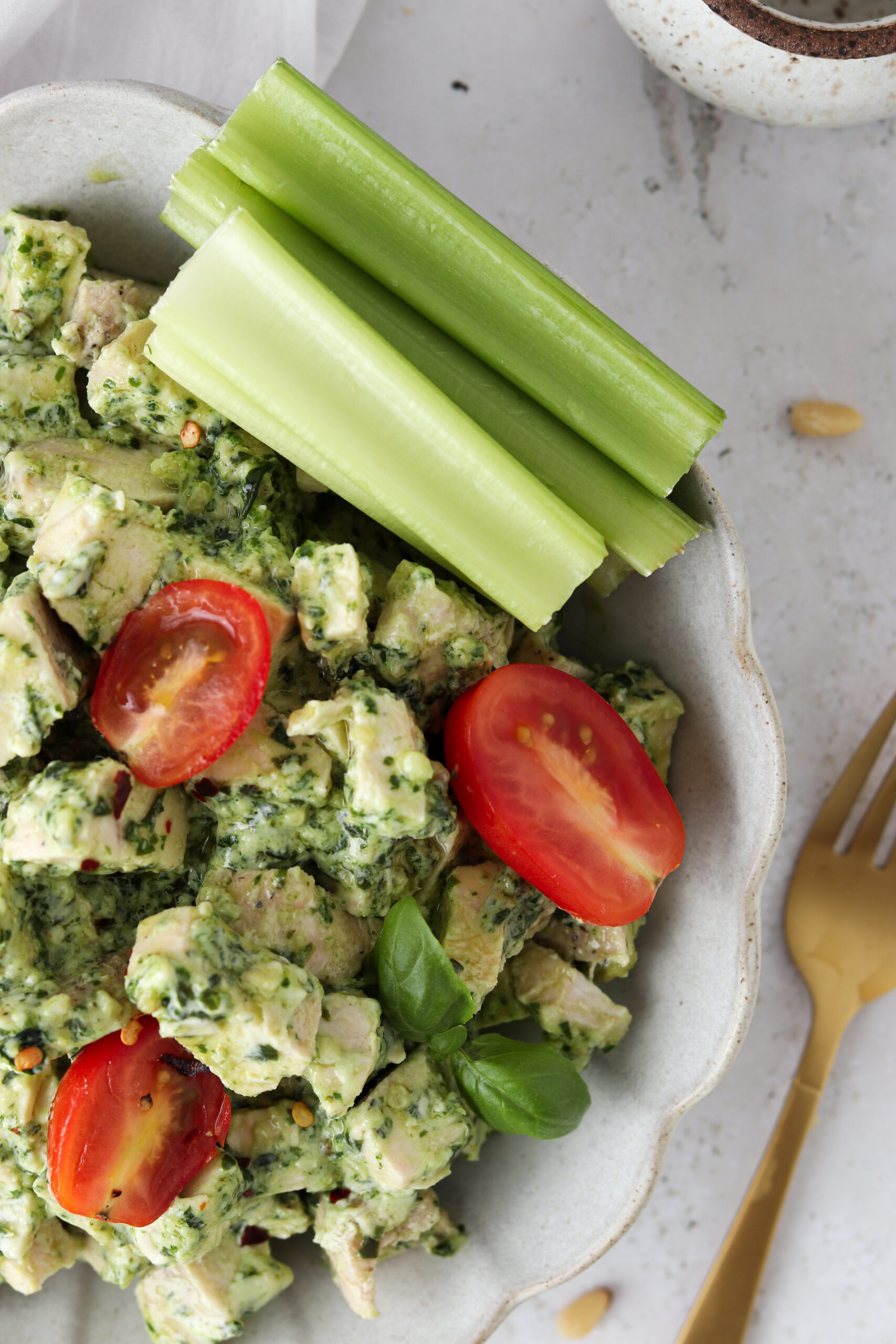 Up close picture of pesto chicken salad in a bowl with celery sticks and halved grape tomatoes. 