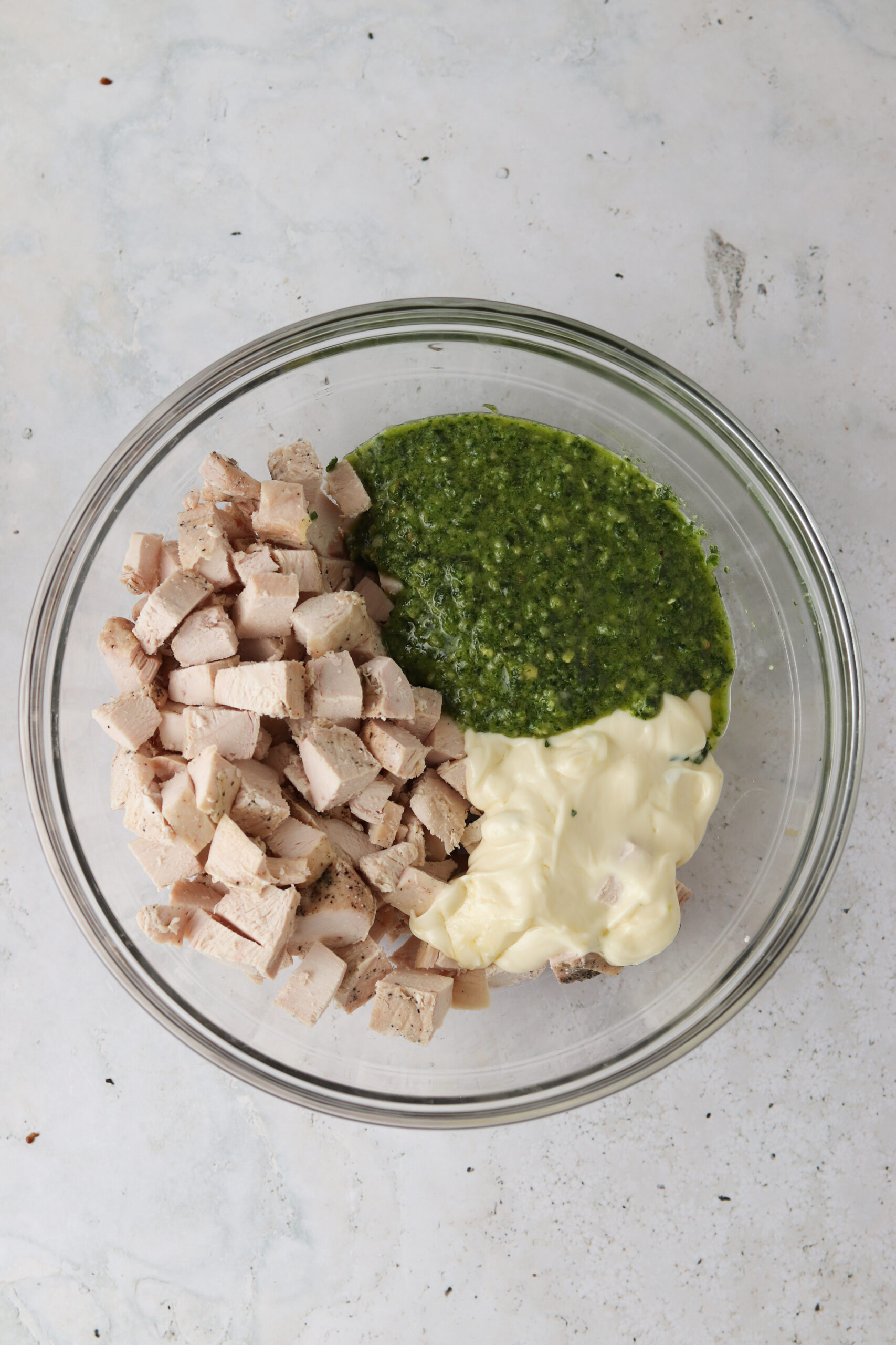 Pesto, cubed chicken, and avocado mayo in a large glass bowl. 