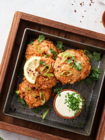 whole30 crab cakes on a black plate with aioli dipping sauce green herb garnish and a lemon wedge