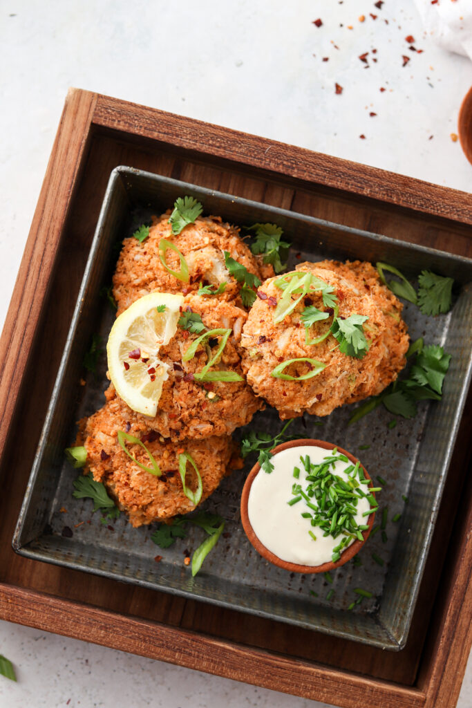 whole30 crab cakes on a black plate with aioli dipping sauce green herb garnish and a lemon wedge