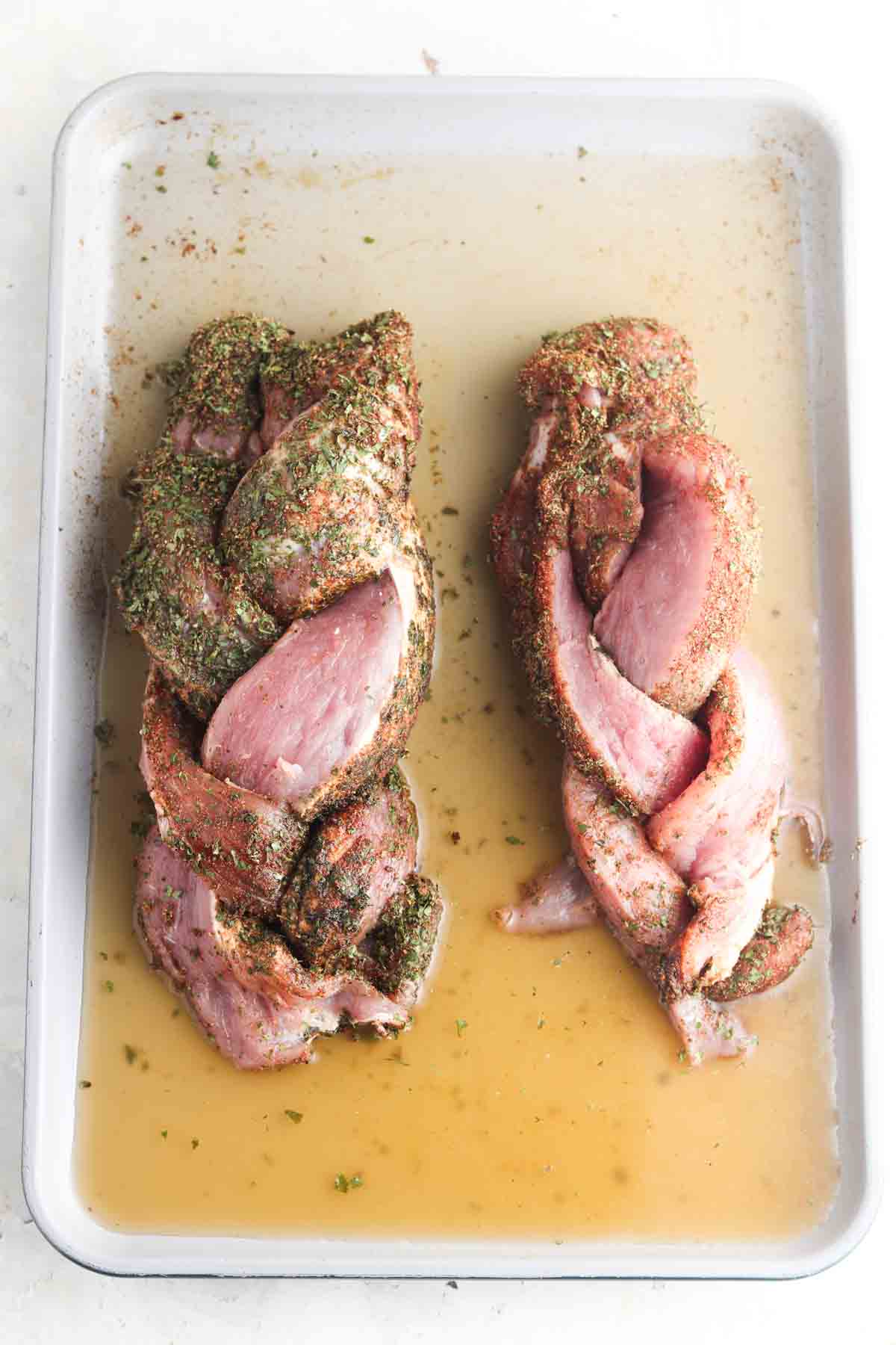 Bone broth poured on a baking sheet with beef tenderloin and herbs. 
