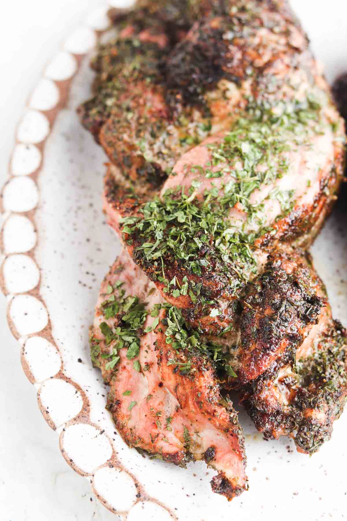 Braided pork tenderloin on a plate with herbs on top.
