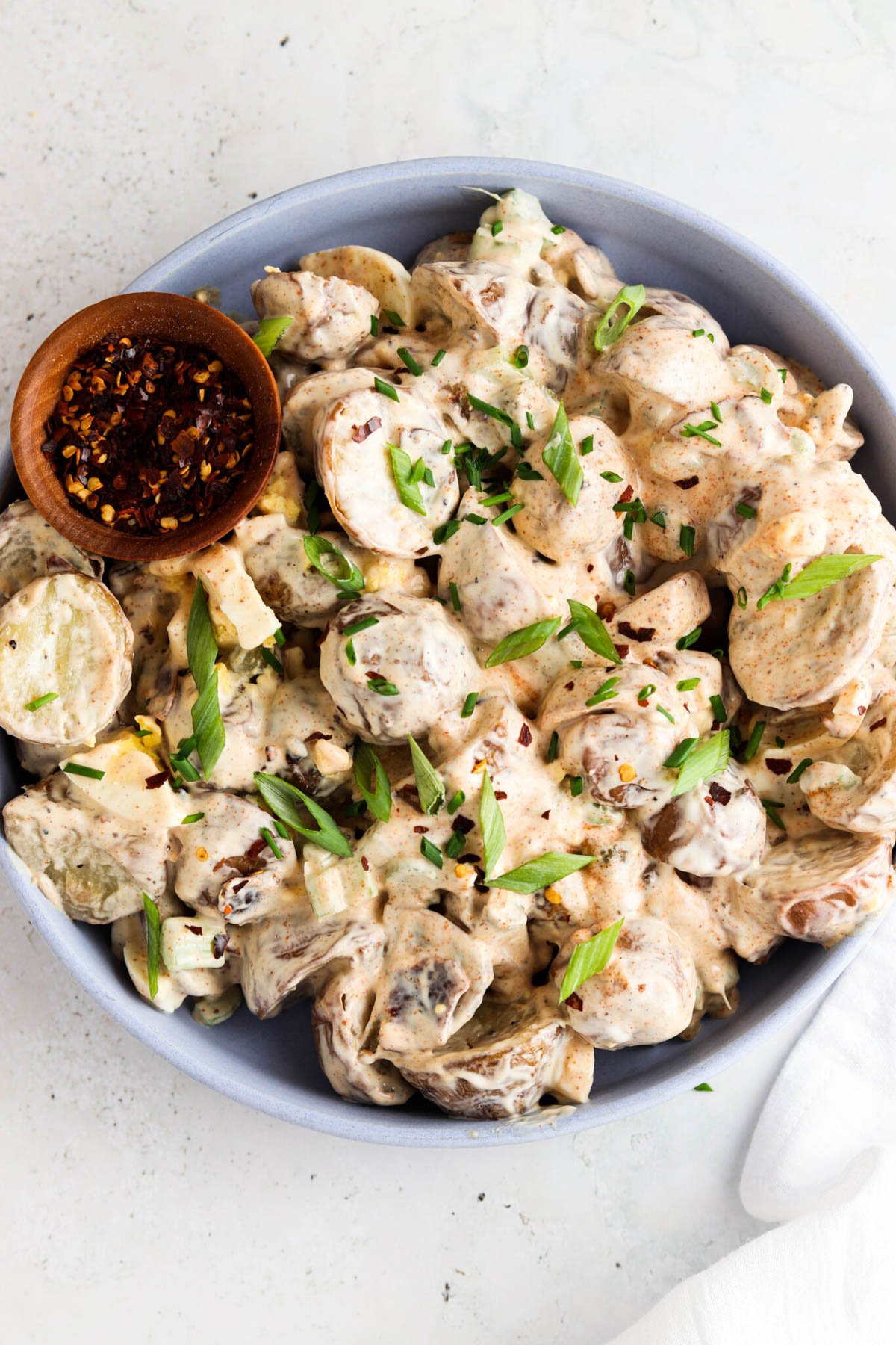 Gluten free potato salad in a blue bowl with green onions and red pepper flakes.