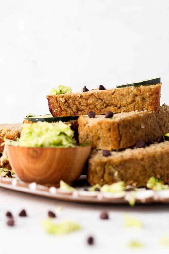 Zucchini bread stacked up on a plate with grated zucchini on the side. 