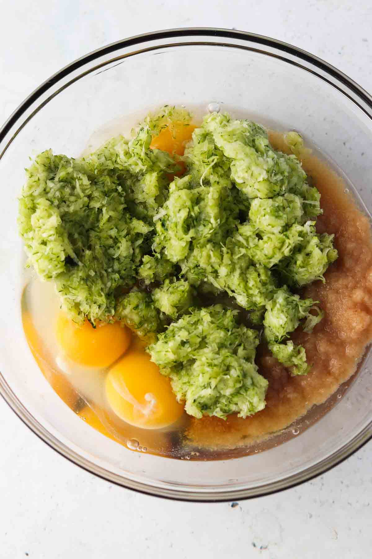 Zucchini, eggs, and applesauce in a large glass bowl.