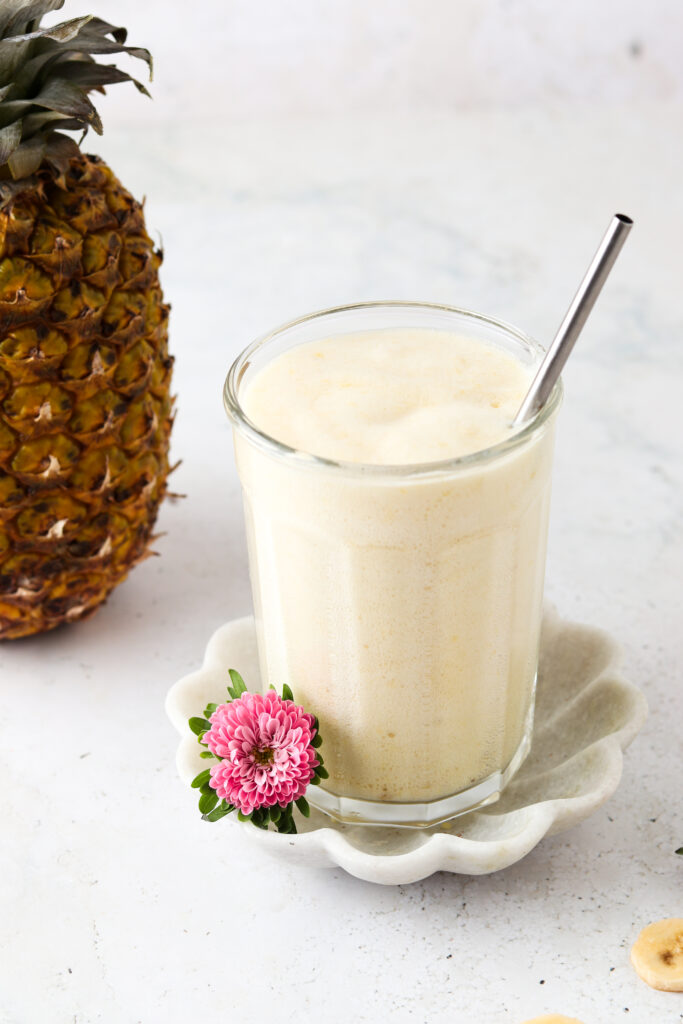 Pretty tropical smoothie in a cup with a pineapple and flower sitting next to it.