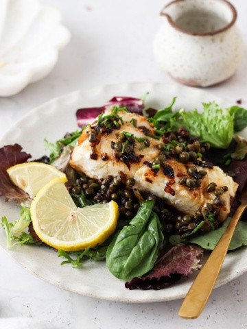 pan seared sea bass on a plate with greens and lemon