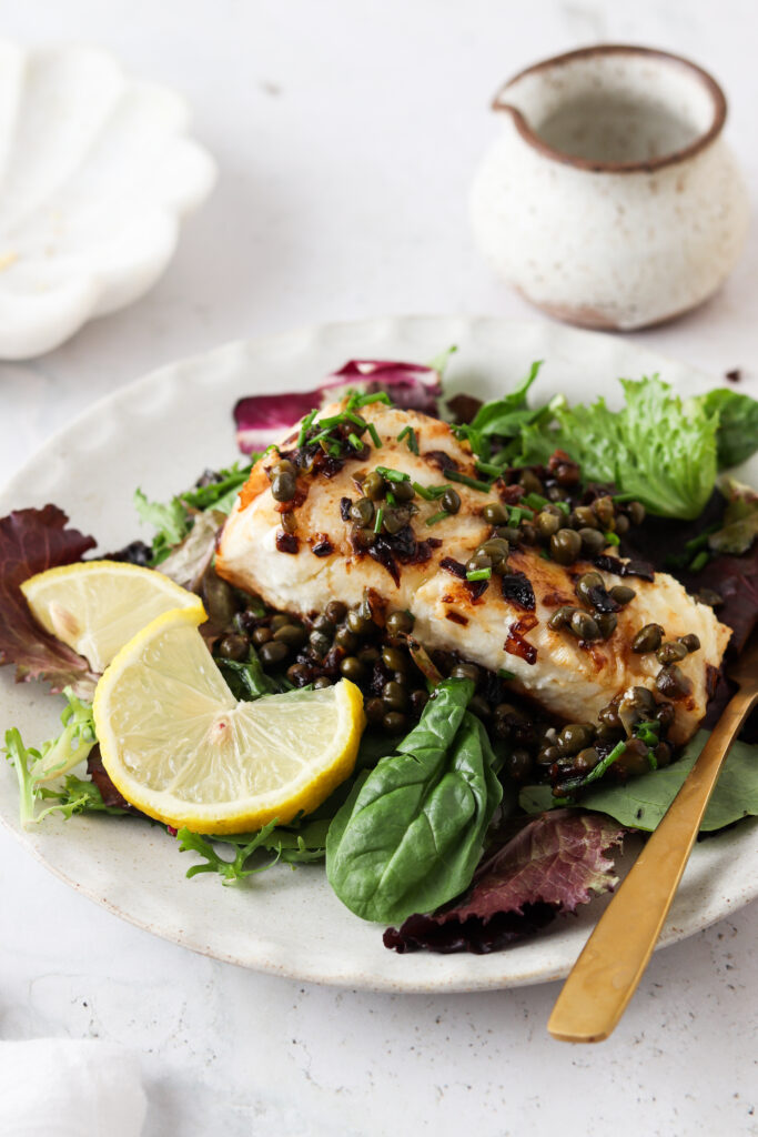 pan seared sea bass on a plate with greens and lemon