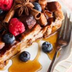Slice of french toast on a plate with a pink napkin under it and fresh berries on top.