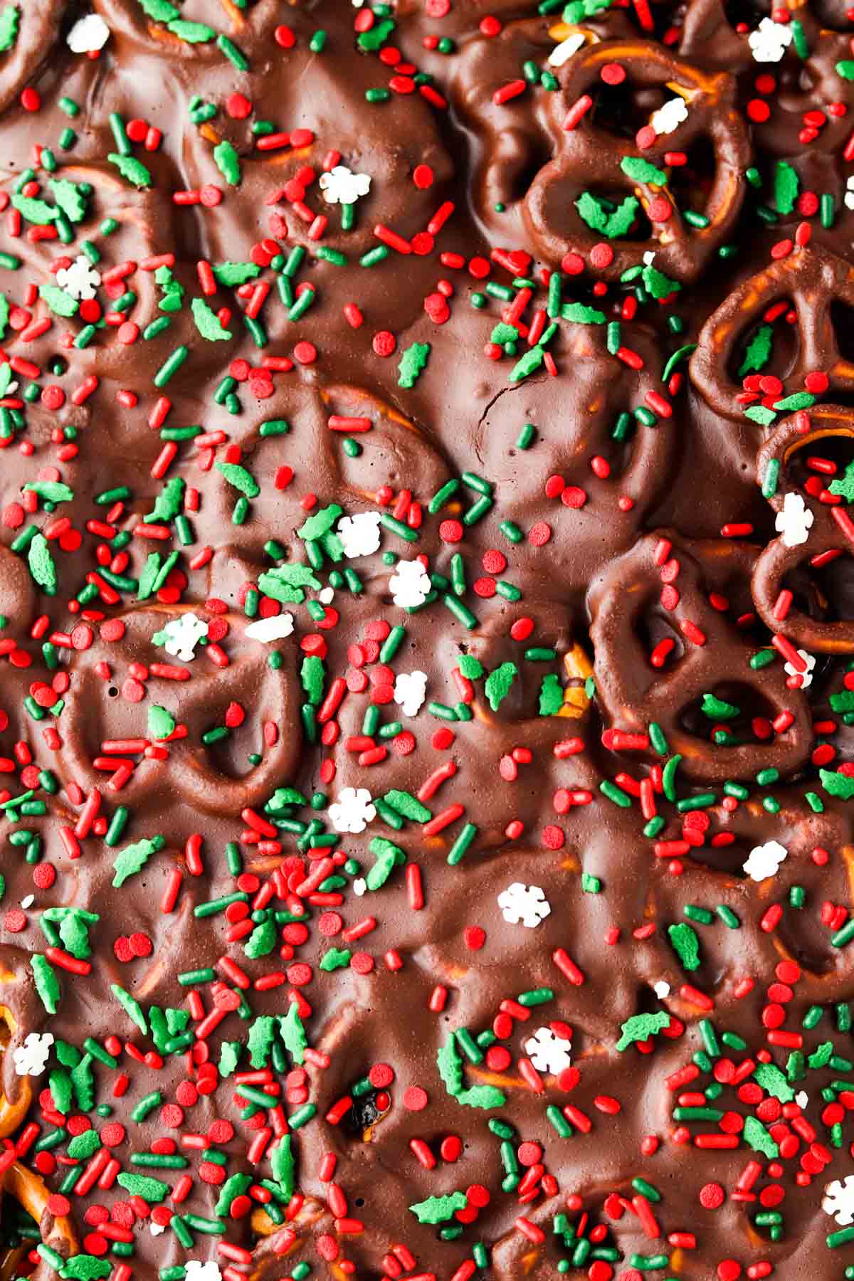 Pretzels with chocolate and christmas sprinkles on top of a sheet pan.
