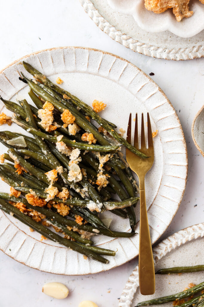 Green bean casserole with pork rinds on top on white plates with a fork.