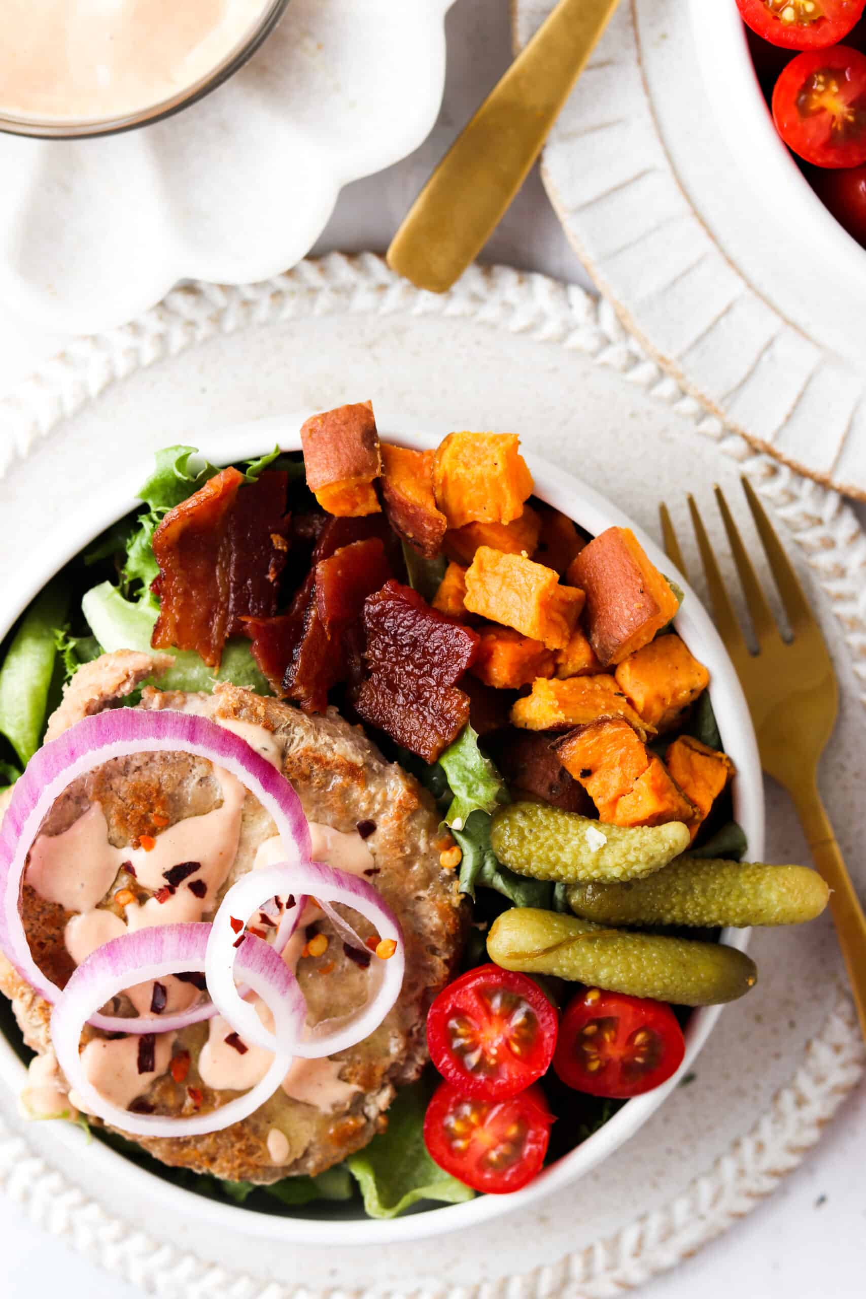 Deconstructed burger bowls with sweet potatoes, pickles, tomatoes, and bacon.