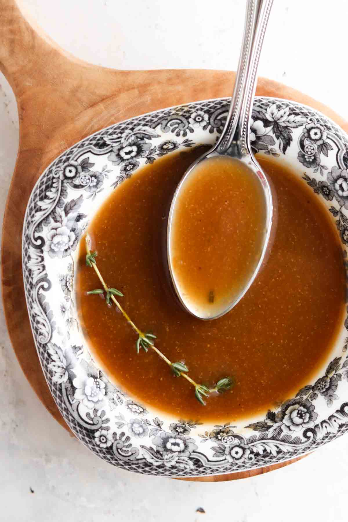 whole30 gravy 7 Dairy free gravy in a black and white bowl with a spoon in it and a piece of fresh thyme.