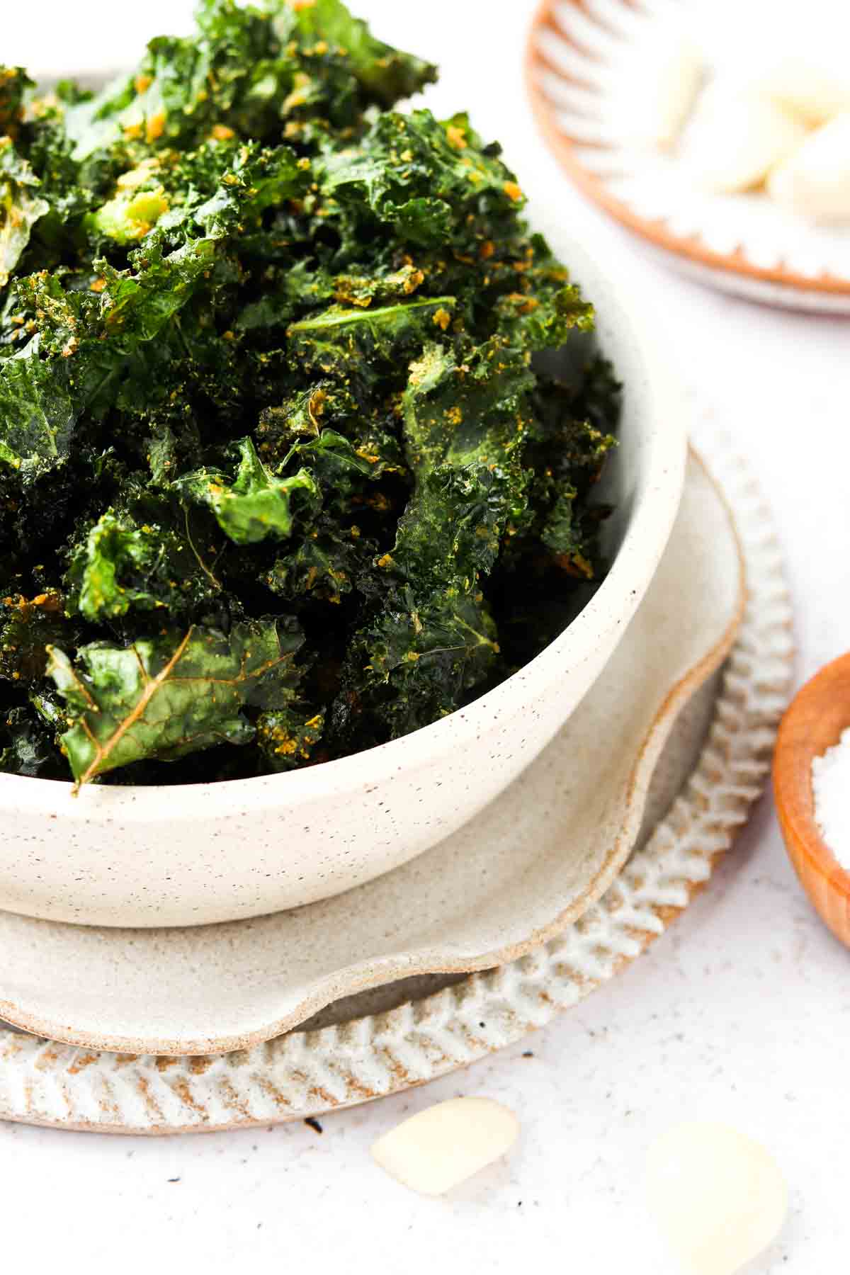 Dehydrated kale chips in a bowl with nutritional yeast on top.