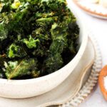 close up photo of dehydrated kale chips in a bowl with nutritional yeast on top