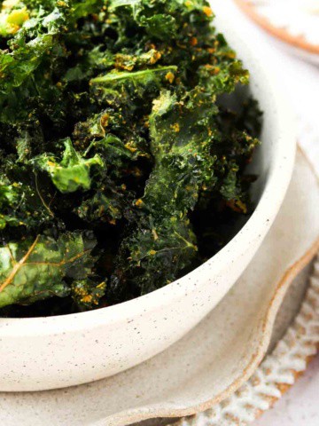 close up photo of dehydrated kale chips in a bowl with nutritional yeast on top