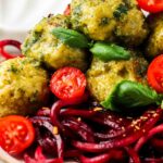 close up photo of meatballs with pesto sauce over beet noodles