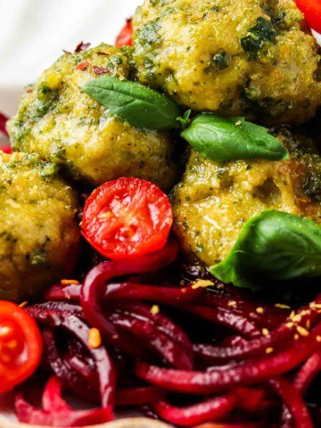 close up photo of meatballs with pesto sauce over beet noodles