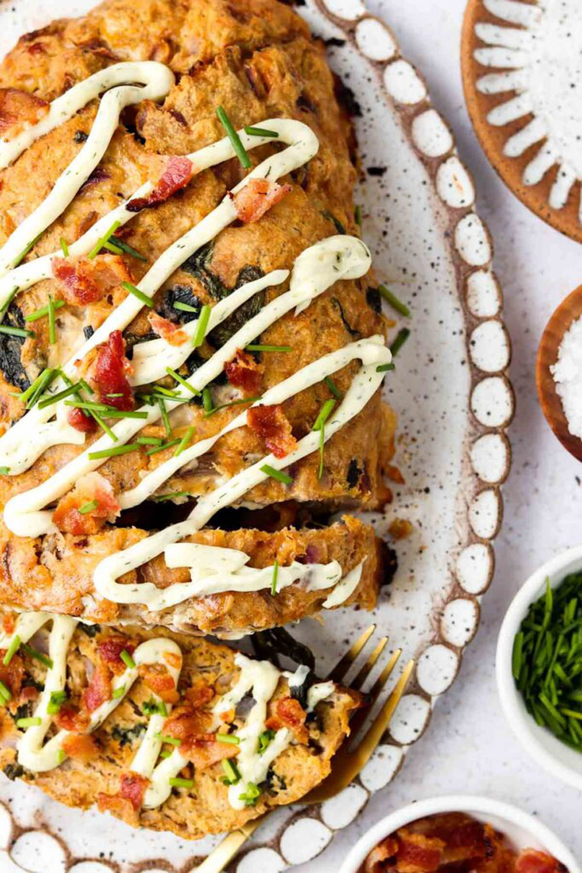 Whole keto meatloaf on a platter with dairy free ranch and bacon crumbles. 