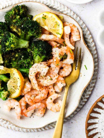 lemon and shrimp with broccoli on a plate with a gold fork