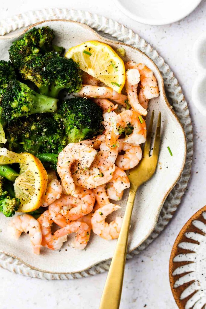 lemon and shrimp with broccoli on a plate with a gold fork