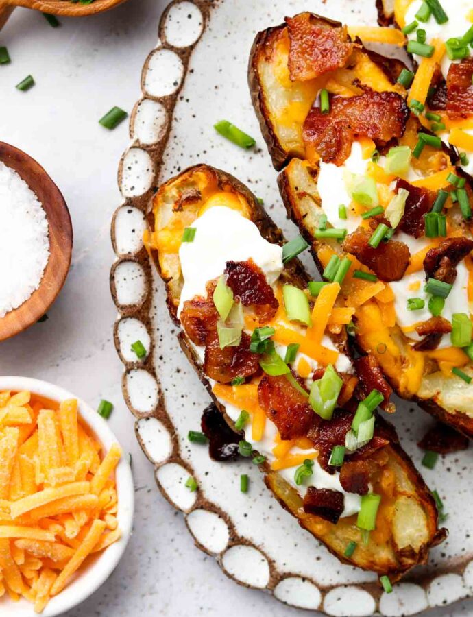 potato skins on a plate with cheese, green onions and sour cream