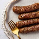 4 sausages on a plate with a gold fork