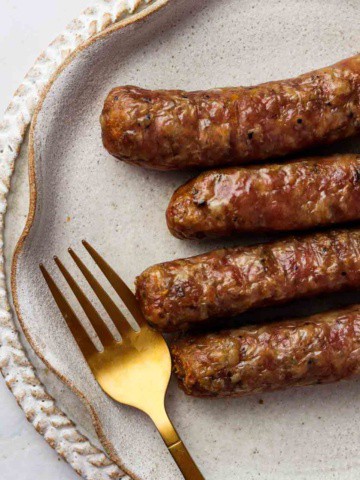 4 sausages on a plate with a gold fork