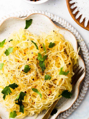 Easy air fryer spaghetti squash on a plate with fresh green herbs.