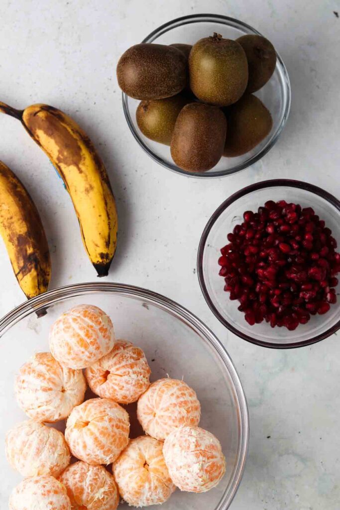 clementines, pomegranate, kiwi and bananas in bowls