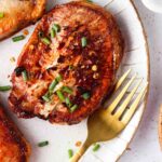 cooked frozen pork chops with chives on top on a white plate with a gold fork