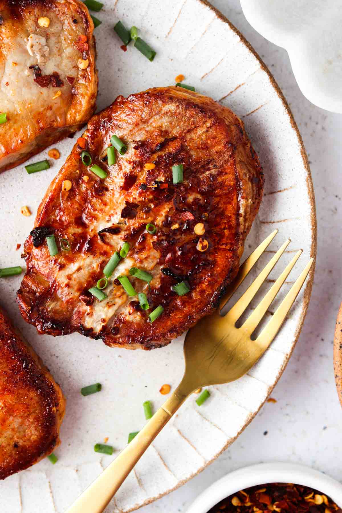 Cooked frozen pork chops with chives on top on a white plate with a gold fork.