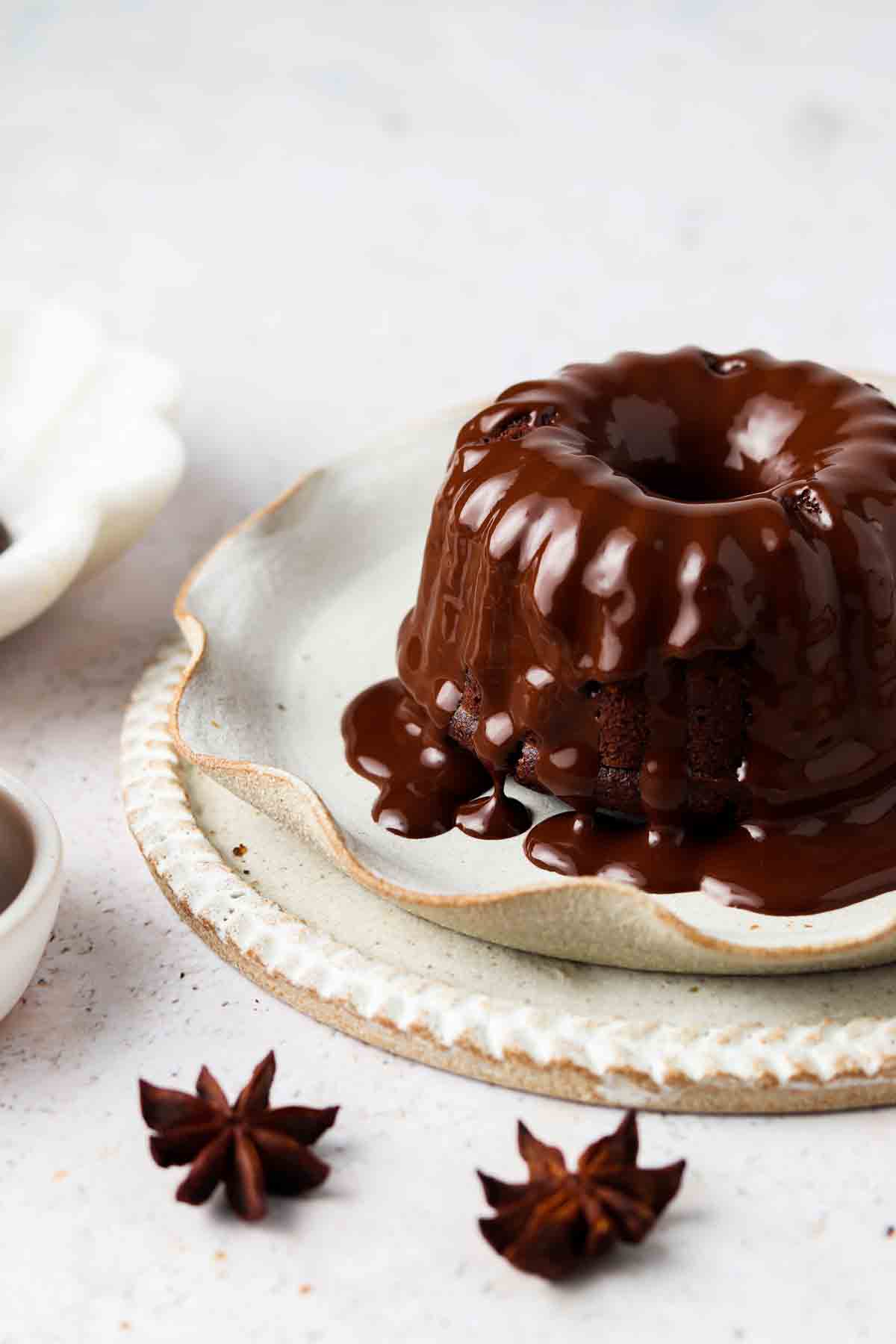 Mini chocolate bundt cake on a plate with silky chocolate ganache on top.