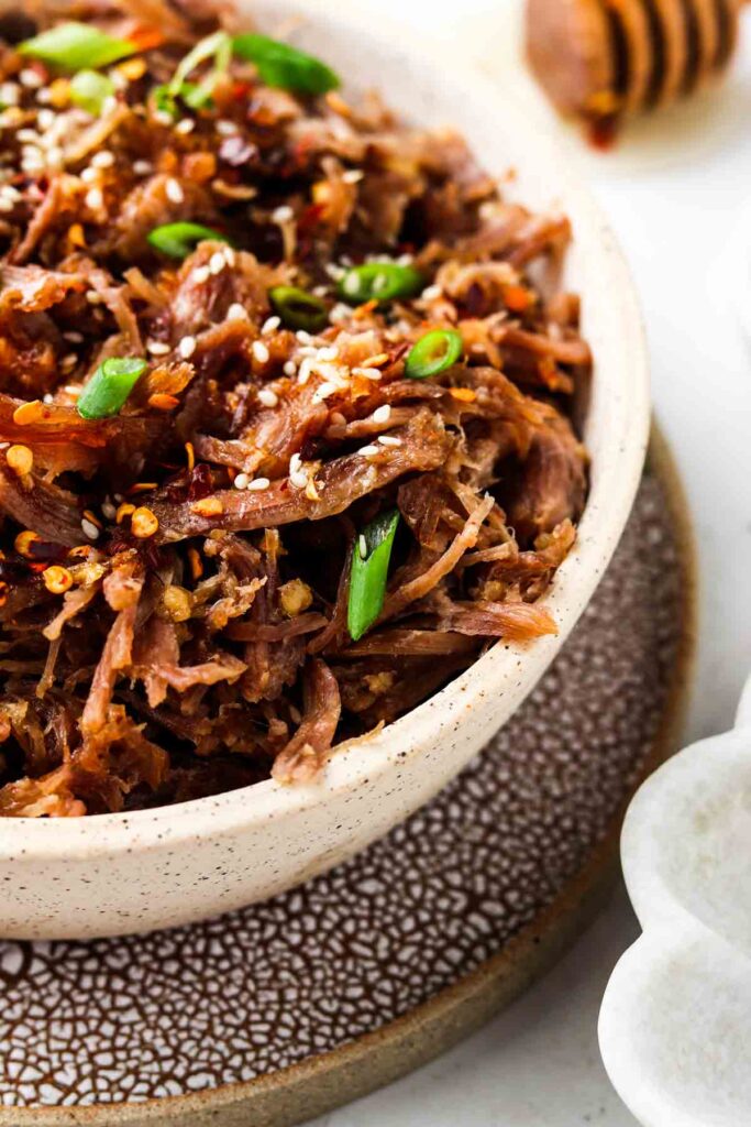 honey pulled pork in a bowl with green onions and sesame seeds on top