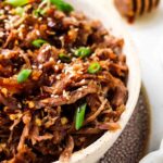 pulled pork in a bowl with green onions and sesame seeds on top