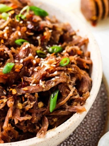 pulled pork in a bowl with green onions and sesame seeds on top