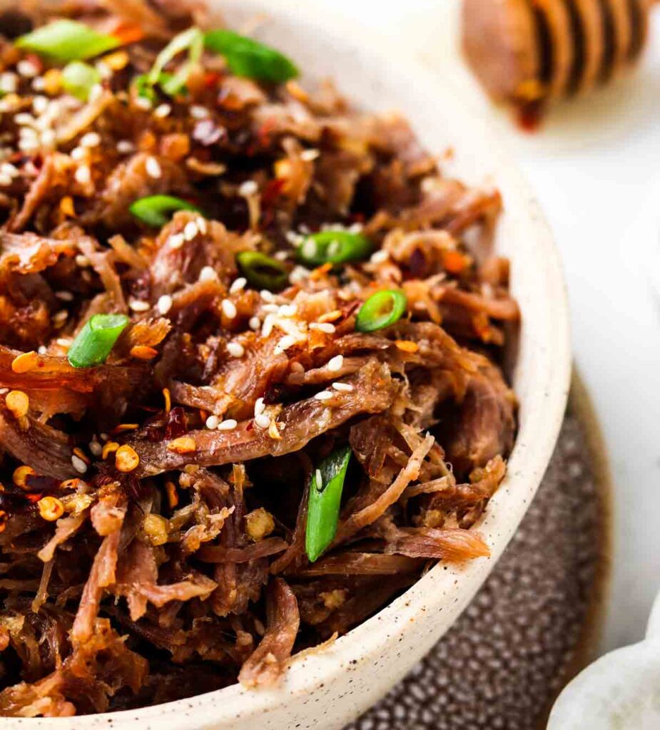 pulled pork in a bowl with green onions and sesame seeds on top