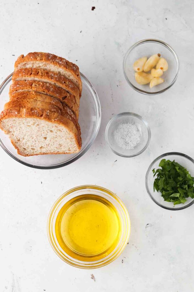 gluten free bread, dairy free butter, sea salt, garlic and fresh parsley all laid out in bowls