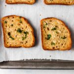 4 slices of gluten free garlic bread with parsley on top on a baking sheet