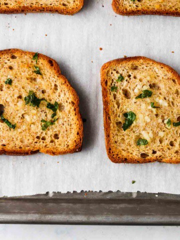 4 slices of gluten free garlic bread with parsley on top on a baking sheet