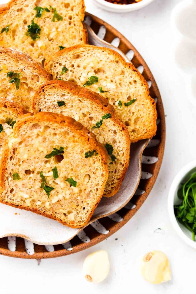 5 slices of gluten free garlic bread on a plate with fresh herbs