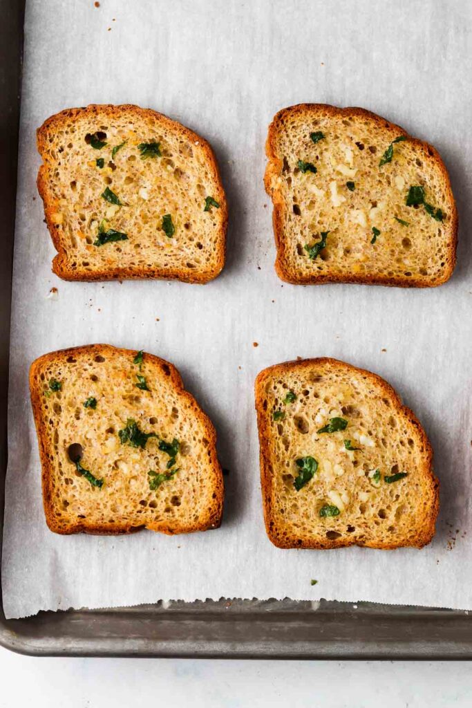 4 slices of gluten free garlic bread with parsley on top on a baking sheet